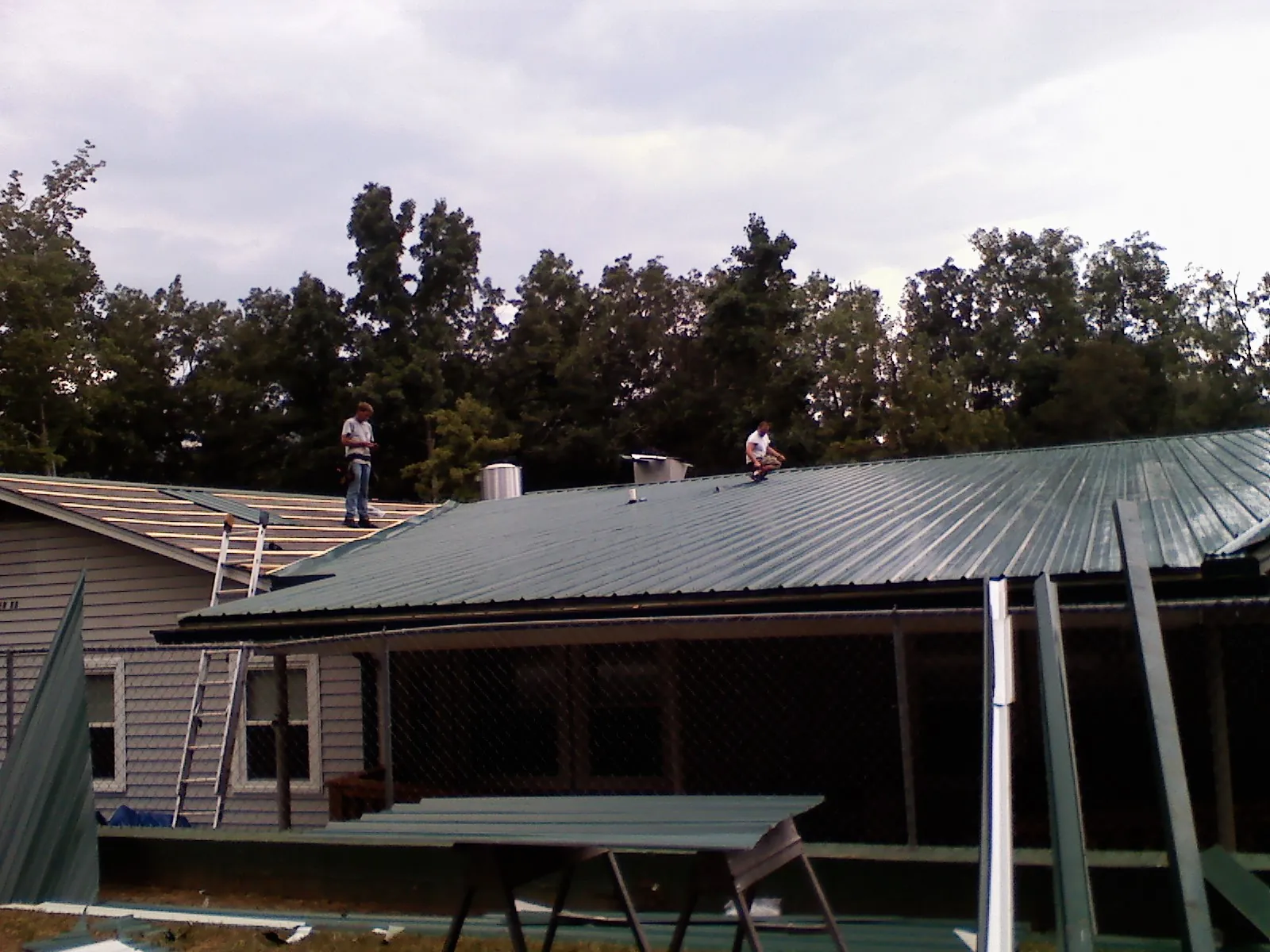Two roofers installing green metal panels above a covered porch in Orlando