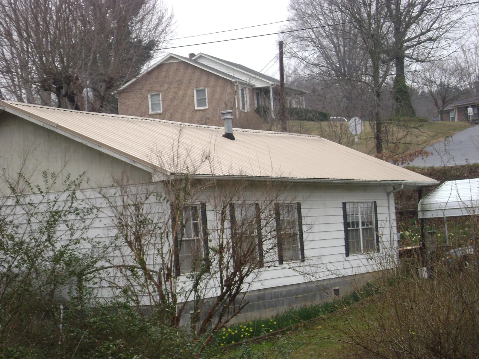 Tan metal roof on a white sided house set into a hillside — Commercial Roofing by Roofing Brothers in Orlando